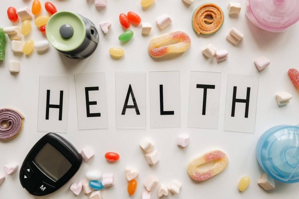 Creative flat lay with sweets around a HEALTH text and monitoring device, symbolizing diabetes awareness.